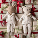 Two plush stuffed toys dressed in matching holiday pajamas, surrounded by wrapped gift boxes with red and green ribbons. The left toy is a reindeer with antlers, and the right toy is a bear, both in cream pajamas with small floral and star prints.