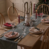 Dining table set for a meal with red candles, greenery, and decorative items.