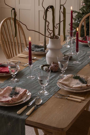 Dining table set for a meal with red candles, greenery, and decorative items.