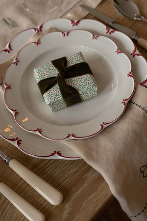 Decorative table setting with a small gift box on a plate, surrounded by cutlery and a napkin.