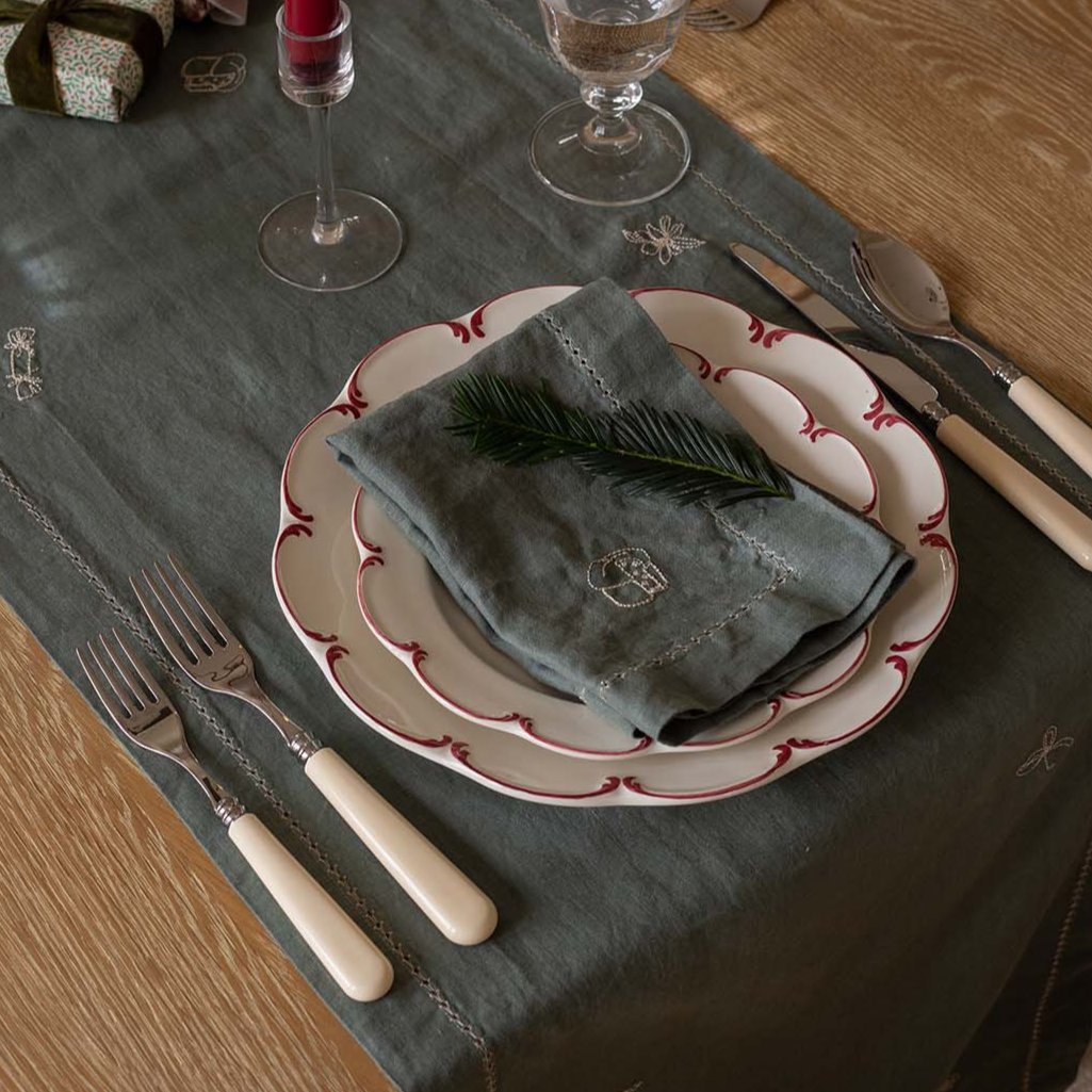 Dining table setting with plates, cutlery, and a napkin on a dark green tablecloth.