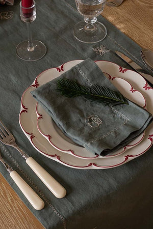 Dining table setting with plates, cutlery, and a napkin on a dark green tablecloth.