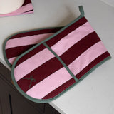 A pair of striped oven mitts with horizontal bands of dusty pink and deep burgundy, finished with sage green trim and handles, resting on a white countertop.