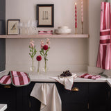 A styled kitchen corner with dark cabinetry, a white countertop, pink striped textiles, framed wall art, glassware, candles, and flowers. No person or animal is present, and the scene appears to be a real interior environment rather than a clean isolated product shot, so this fits Lifestyle rather than Product/Packaging.