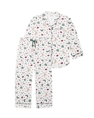 A two-piece pajama set featuring a long-sleeve button-front top and matching pants in an off-white base with a festive Christmas print of reindeer, candy canes, pine trees, and snowflakes, accented with dark green piping and a dark green drawstring.