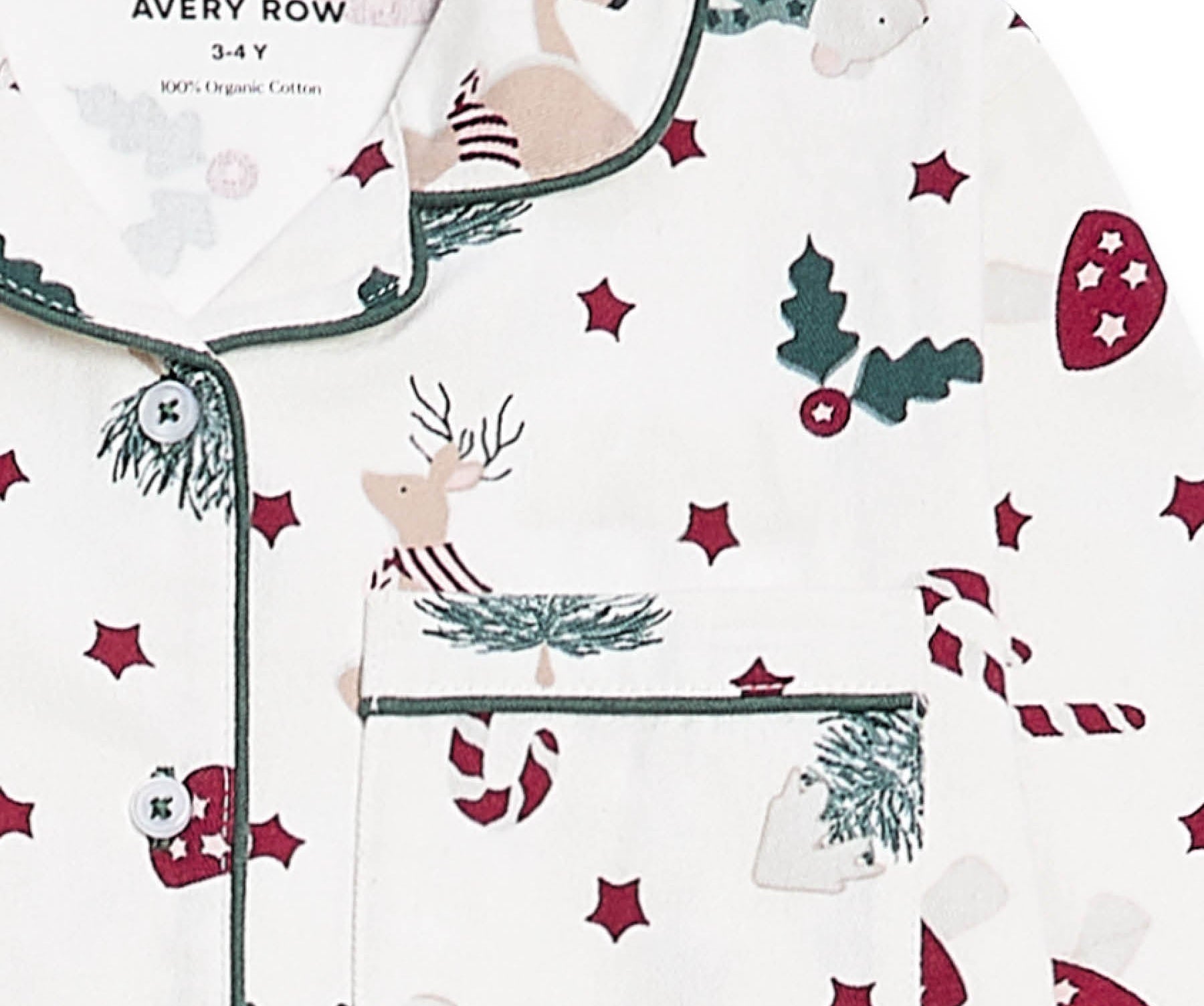 A close-up of a white long-sleeve pajama top with a Christmas print, featuring green piping, a chest pocket, and motifs of reindeer, candy canes, mistletoe, and red stars. The brand name 'AVERY ROW' is visible on the inner neck label.