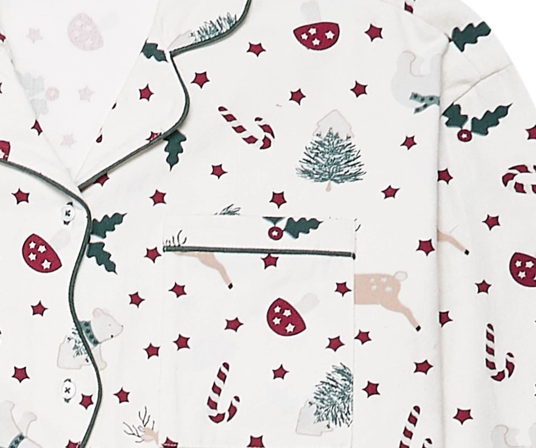 A close-up of a pajama top with a festive Christmas print on an off-white background. The pattern features dark green holly leaves, red candy canes, red stars, beige reindeer, and green Christmas trees.