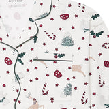 A close-up of a pajama top with a festive Christmas print on an off-white background. The pattern features dark green holly leaves, red candy canes, red stars, beige reindeer, and green Christmas trees.
