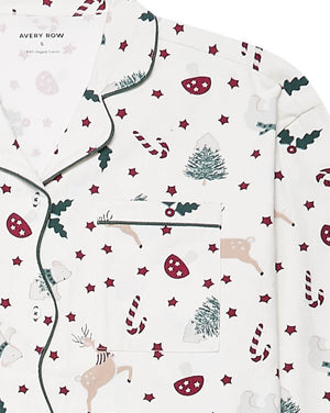 A close-up of a pajama top with a festive Christmas print on an off-white background. The pattern features dark green holly leaves, red candy canes, red stars, beige reindeer, and green Christmas trees.