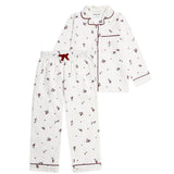 A two-piece children's pajama set featuring a white long-sleeve button-front top and matching pants, both printed with small red cherries and dots, finished with red piping and a red drawstring.