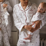 A woman and a baby wearing matching white pajamas with a small red and green floral print. The pajama set has red piping and the word 'Freddie' is embroidered on the chest pocket.