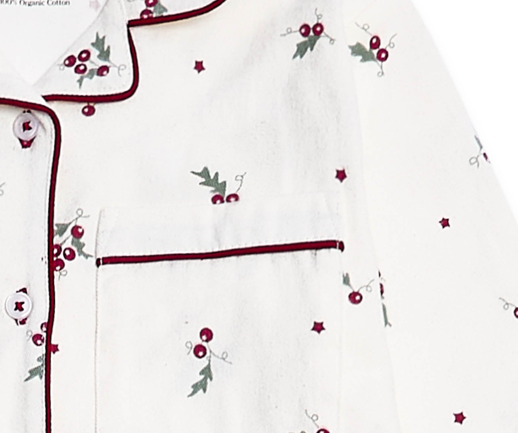 White long-sleeve pajama top with dark red piping, featuring a chest pocket and an all-over holly and berry print with small star accents.