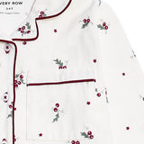 White long-sleeve pajama top with dark red piping, featuring a chest pocket and an all-over holly and berry print with small star accents.