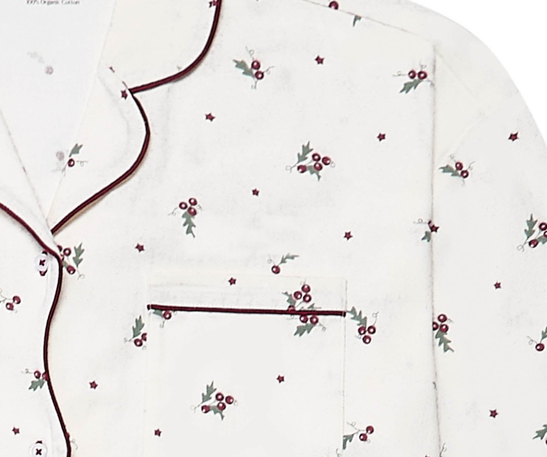A close-up of a white long-sleeve pajama top by Avery Row, featuring a delicate all-over print of small red berries with green leaves and dark burgundy piping along the collar, placket, and pocket.