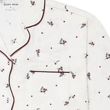A close-up of a white long-sleeve pajama top by Avery Row, featuring a delicate all-over print of small red berries with green leaves and dark burgundy piping along the collar, placket, and pocket.