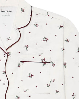 A close-up of a white long-sleeve pajama top by Avery Row, featuring a delicate all-over print of small red berries with green leaves and dark burgundy piping along the collar, placket, and pocket.