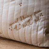 A close-up of a cream-colored quilted pillow with brown embroidered text reading 'special delivery from The North Pole' and small star motifs, resting on a wooden surface.