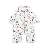 A baby long-sleeve footless romper pajama with a festive Christmas print featuring deer, candy canes, holly, and pine trees on a white background, with green piping trim.