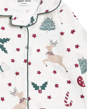 A close-up of a baby pajama top by Avery Row, featuring a festive Christmas print with a beige deer, green trees and holly, and red stars on an off-white background.