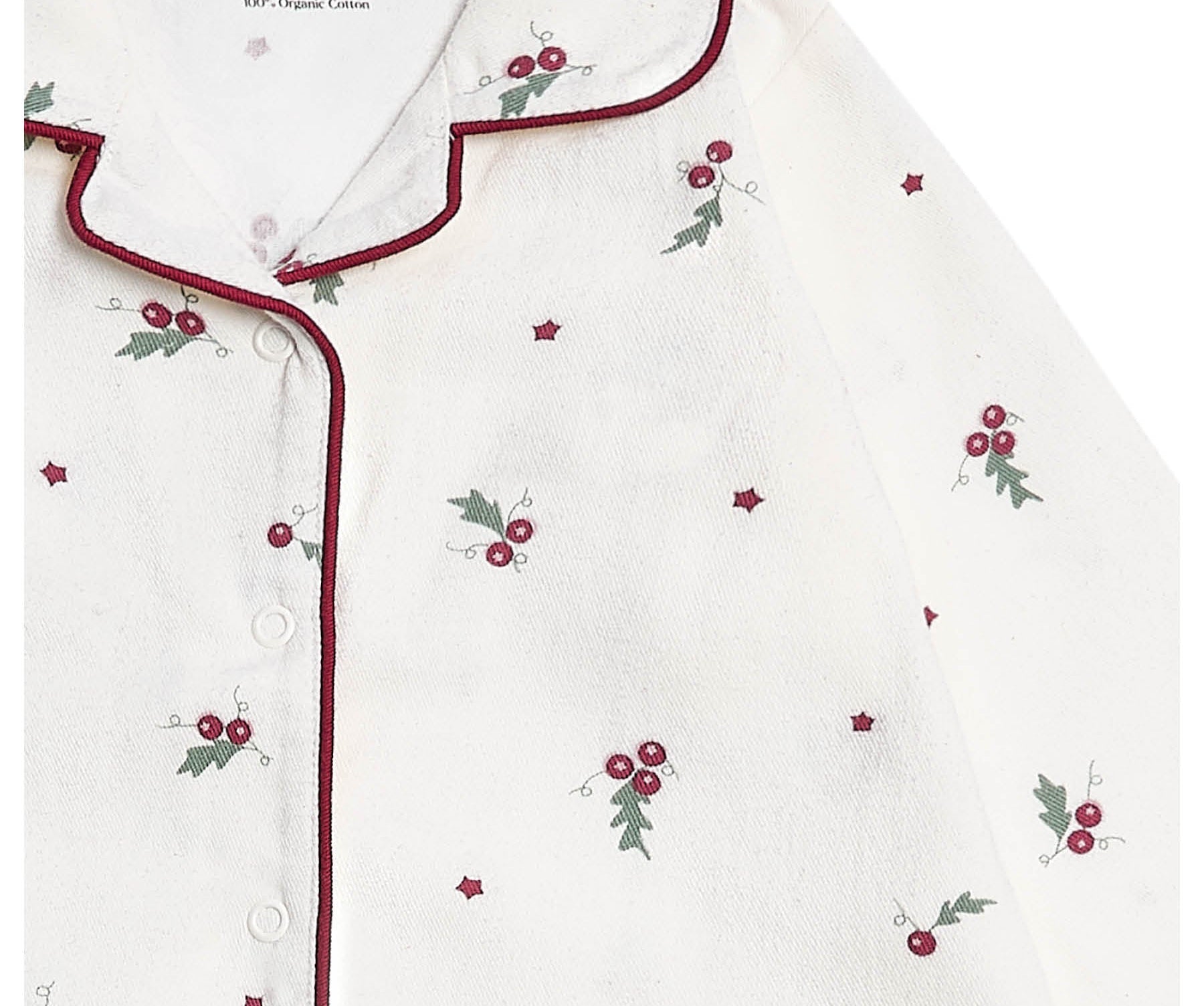 A close-up of a white button-front pajama top by Avery Row, featuring a small red berry and green holly leaf print scattered across the fabric, with dark red piping along the collar and placket.