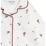 A close-up of a white button-front pajama top by Avery Row, featuring a small red berry and green holly leaf print scattered across the fabric, with dark red piping along the collar and placket.