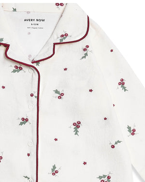 A close-up of a white button-front pajama top by Avery Row, featuring a small red berry and green holly leaf print scattered across the fabric, with dark red piping along the collar and placket.