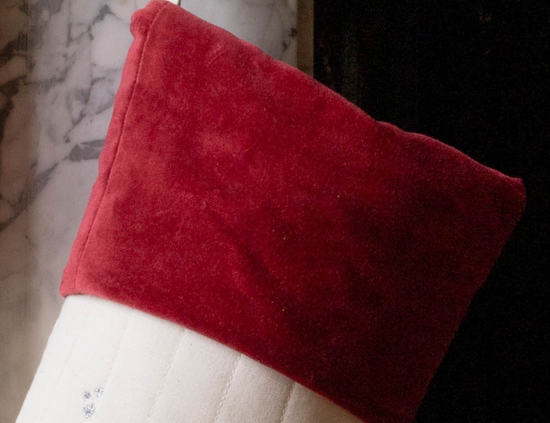 A Christmas stocking with a red velvet cuff and a white body decorated with small holiday illustrations, hanging in front of a fireplace.