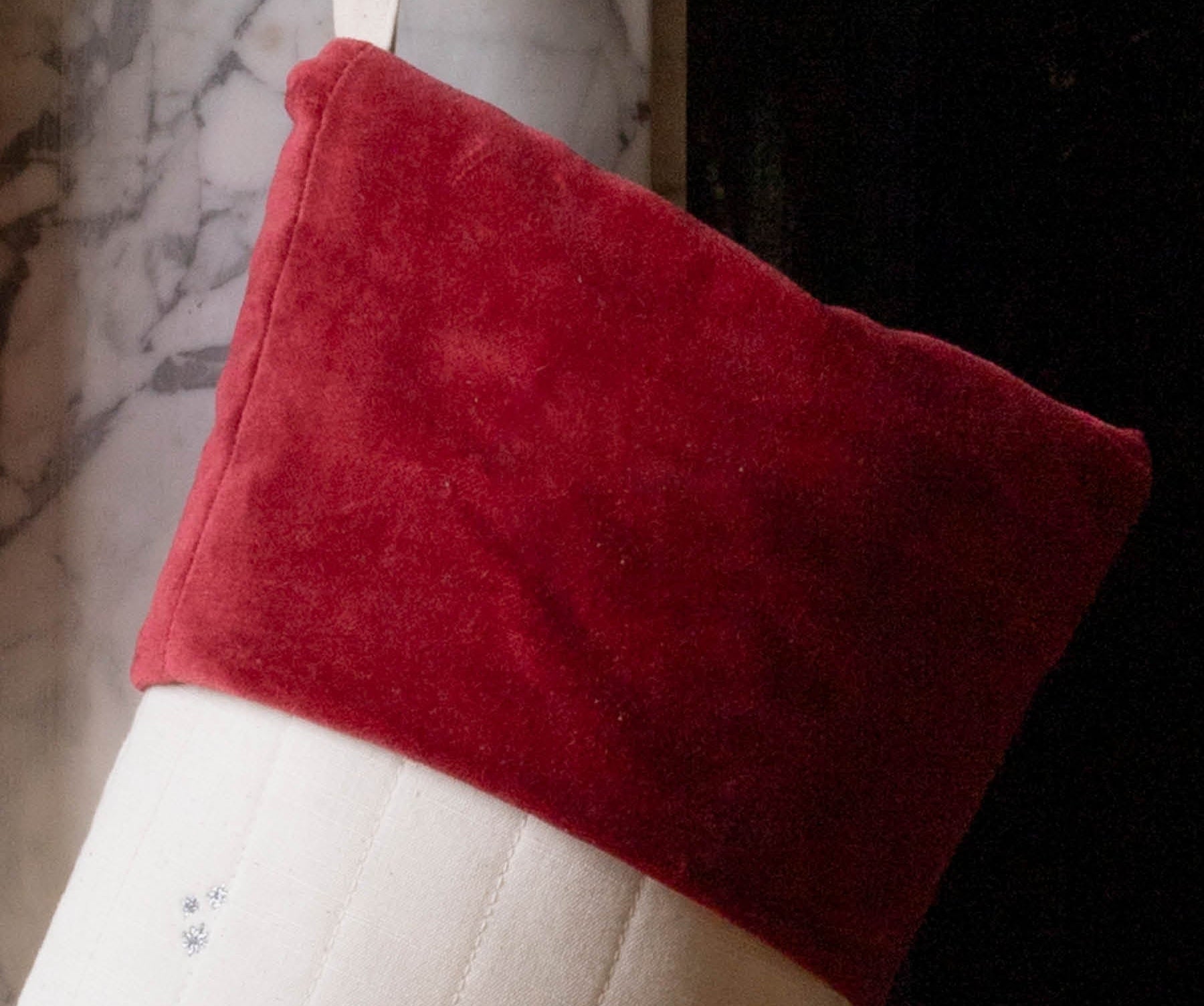 A Christmas stocking with a red velvet cuff and a white body decorated with small holiday illustrations, hanging in front of a fireplace.
