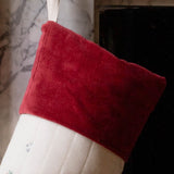 A Christmas stocking with a red velvet cuff and a white body decorated with small holiday illustrations, hanging in front of a fireplace.