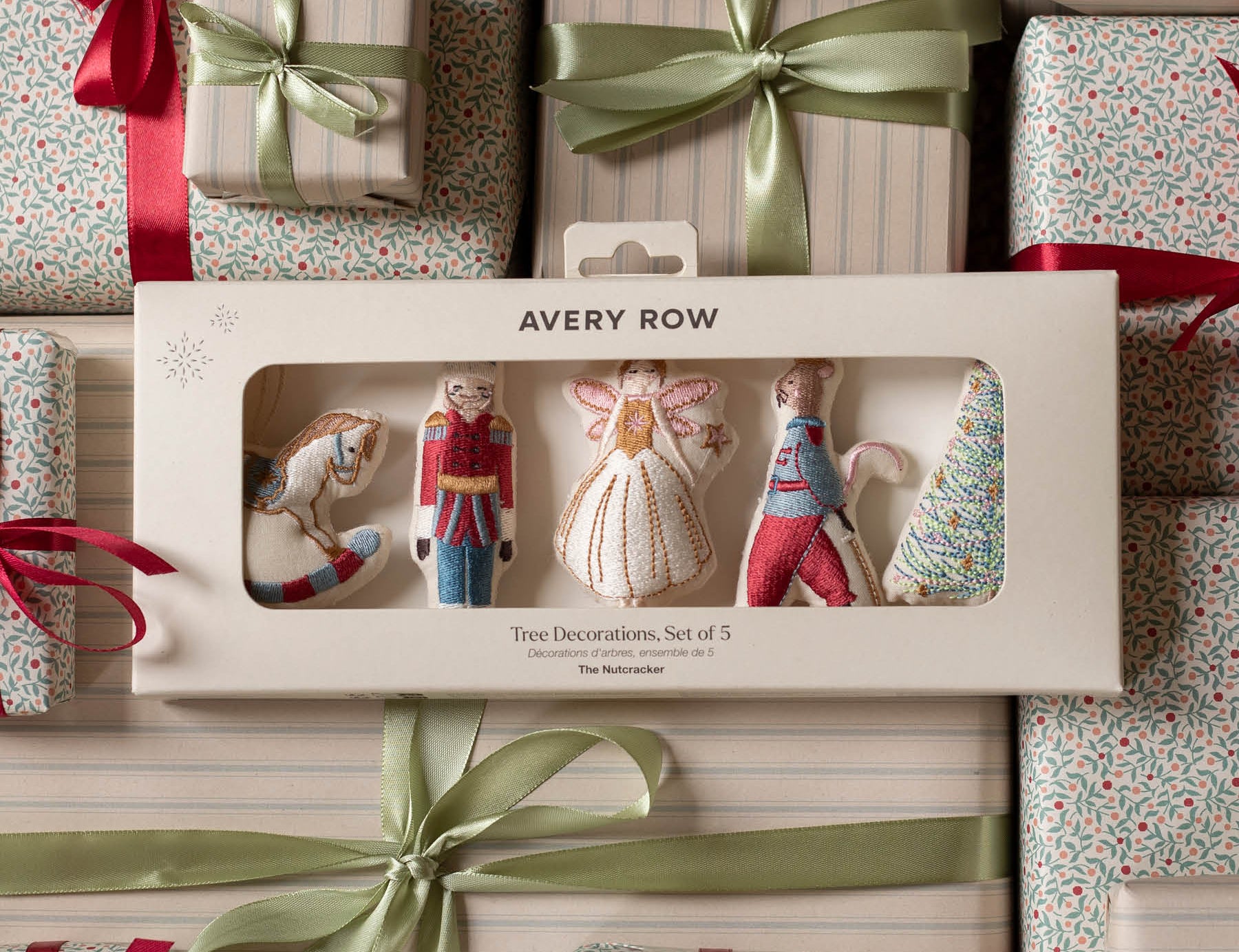 Avery Row Two Decorations Set of 5 in its original window box packaging, surrounded by wrapped Christmas gifts with red ribbons and green satin bows.