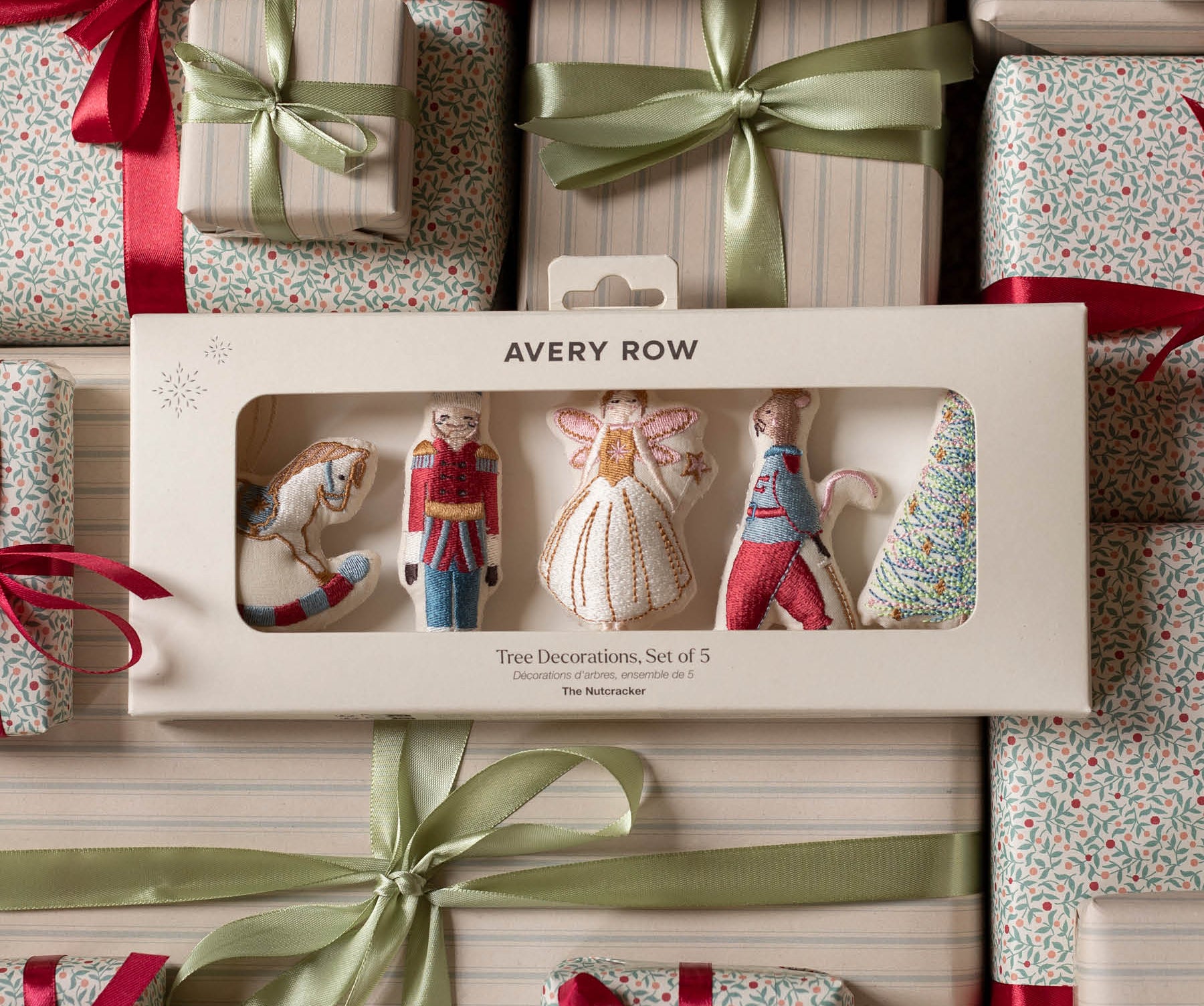 Avery Row Two Decorations Set of 5 in its original window box packaging, surrounded by wrapped Christmas gifts with red ribbons and green satin bows.