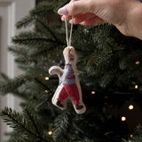 A hand hanging a small handmade felt Christmas ornament shaped like a person in a striped sweater and red pants on a decorated Christmas tree.
