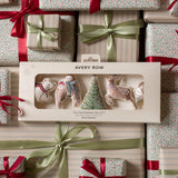 Avery Row Christmas tree decorations set of 5 in a cream-colored gift box, displayed on top of wrapped gift boxes with red ribbons and green satin bows.