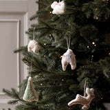 Handmade ceramic Christmas ornaments hanging on a decorated Christmas tree, including a tree-shaped ornament, a snowman, a rabbit, and a deer, with warm string lights in the background.