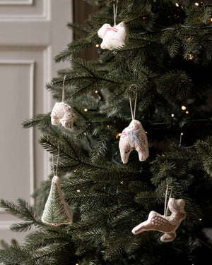 Handmade ceramic Christmas ornaments hanging on a decorated Christmas tree, including a tree-shaped ornament, a snowman, a rabbit, and a deer, with warm string lights in the background.
