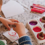 Child's hands with a piece of paper and crayons on a floral-patterned surface
