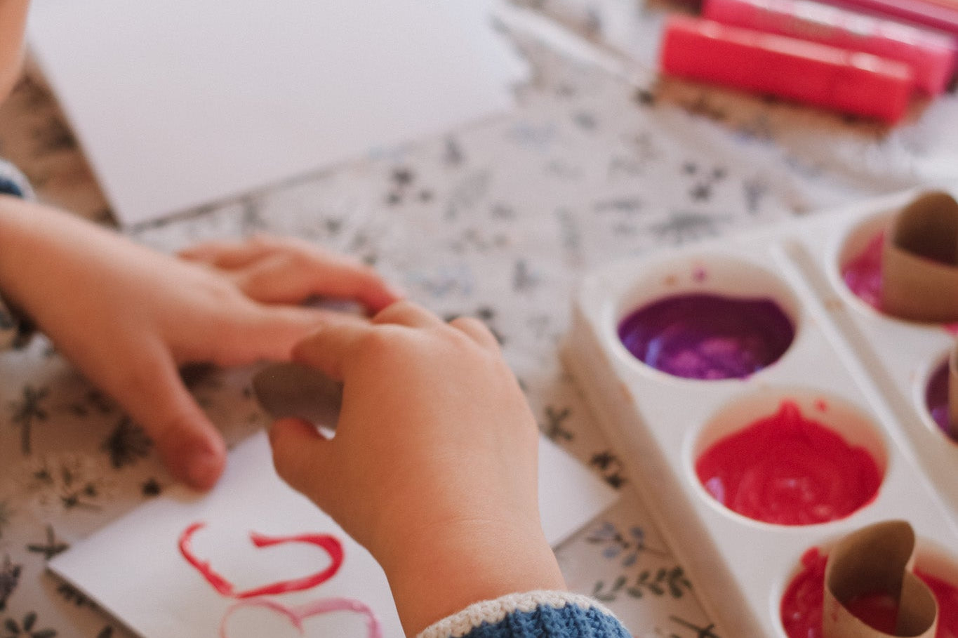 Child's hands with a piece of paper and crayons on a floral-patterned surface
