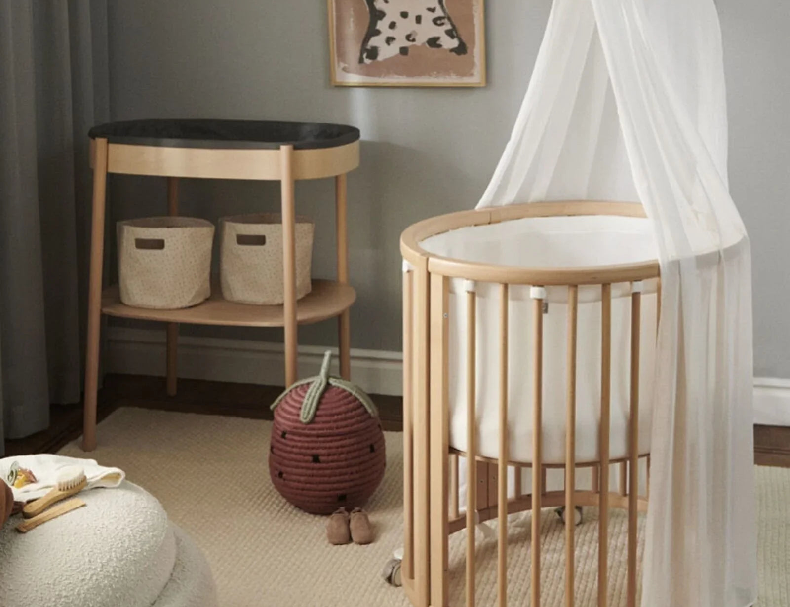 Stokke Sleepi Drape Rod Natural on a round wooden cot with a sheer white drape, in a nursery with a changing table