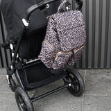 Leopard print backpack attached to a black stroller on a tiled floor.
