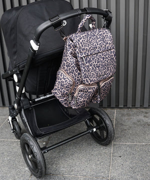 Leopard print backpack attached to a black stroller on a tiled floor.