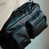 Black bag with visible brand name held by a person against a neutral background