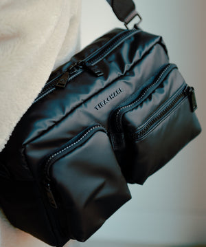Black bag with visible brand name held by a person against a neutral background