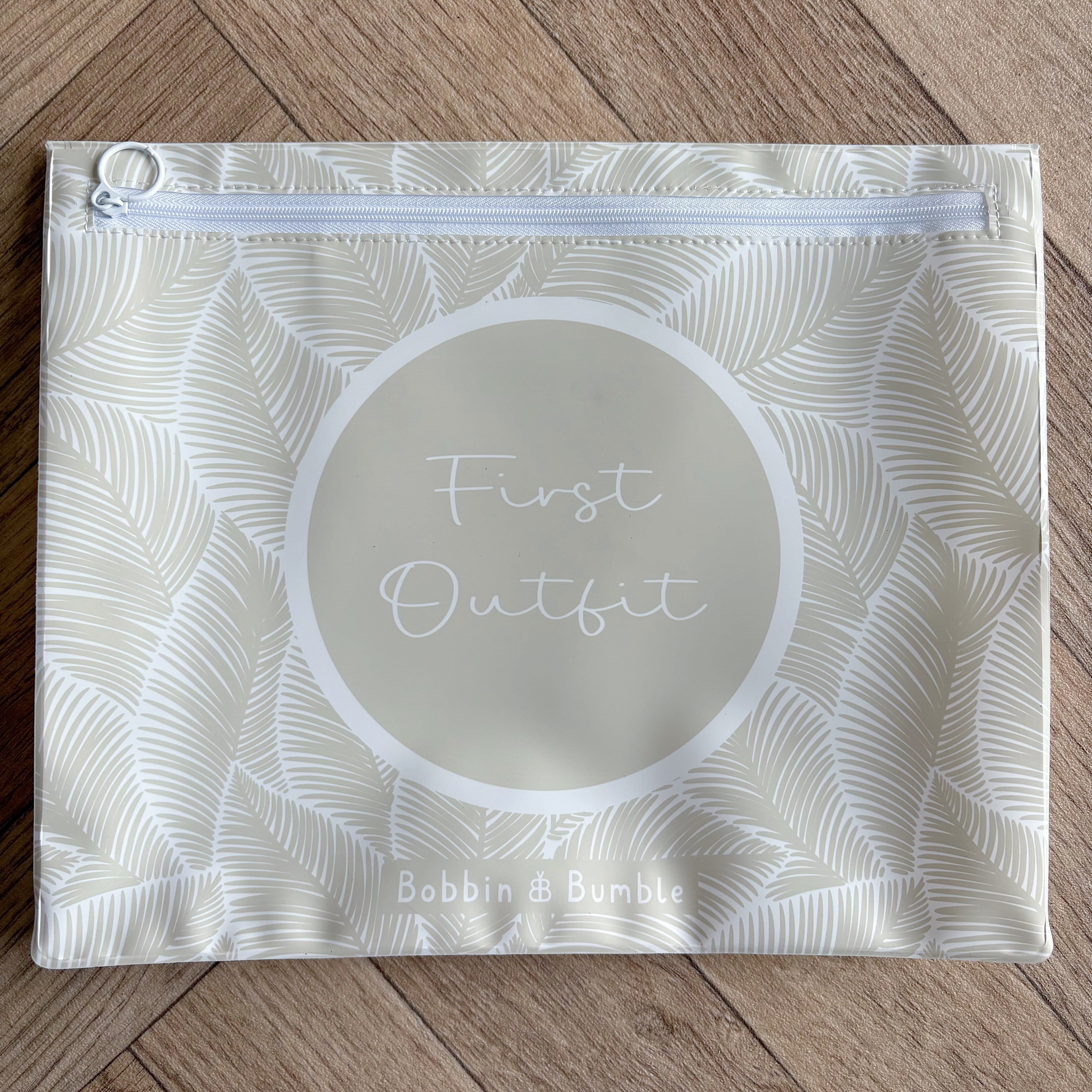 Hospital bag organiser pouches, beige leaf, flat pouch labelled First Outfit on a wooden floor