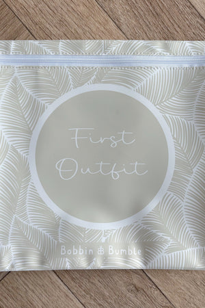 Hospital bag organiser pouches, beige leaf, flat pouch labelled First Outfit on a wooden floor