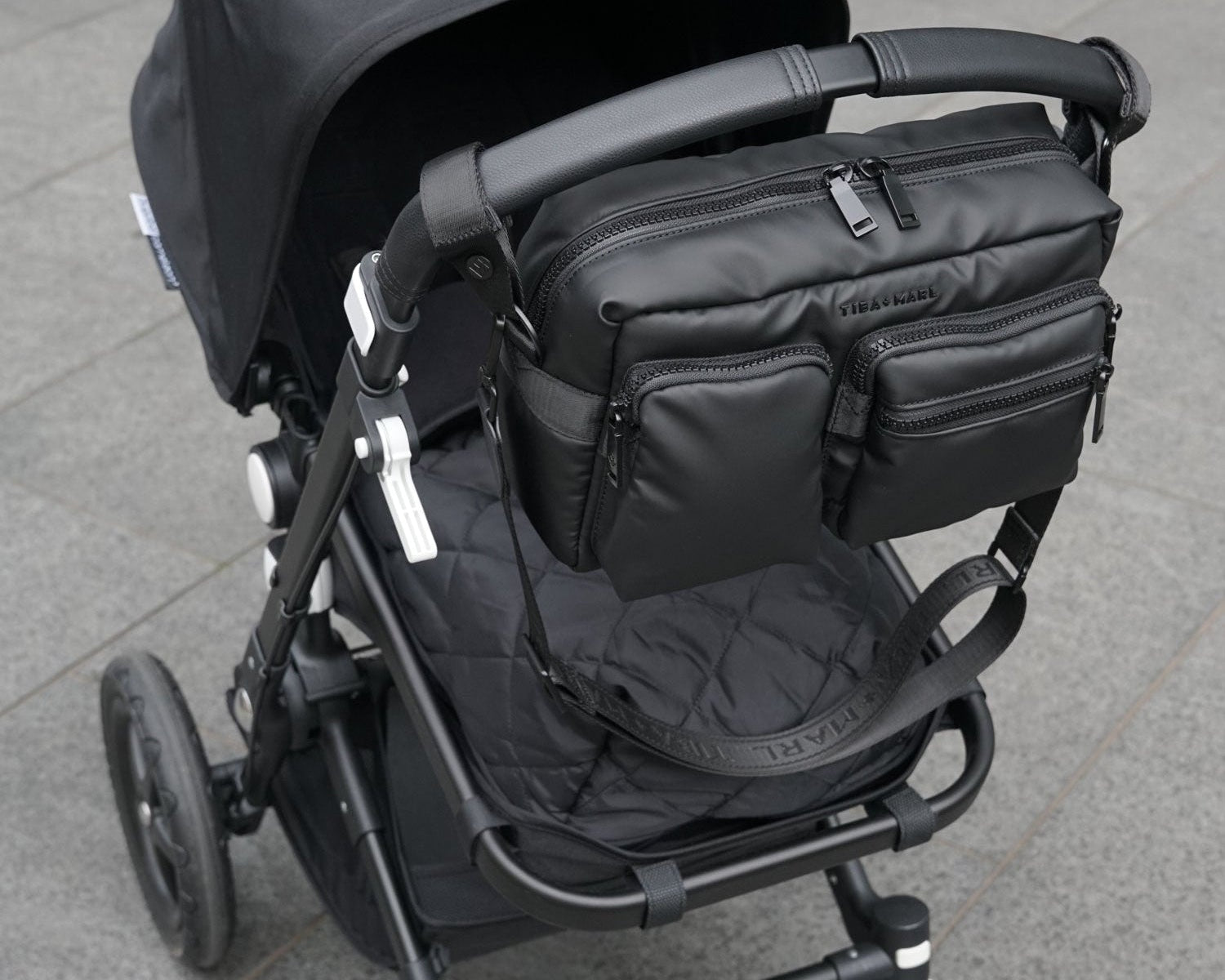 Black stroller with attached bag on a gray pavement