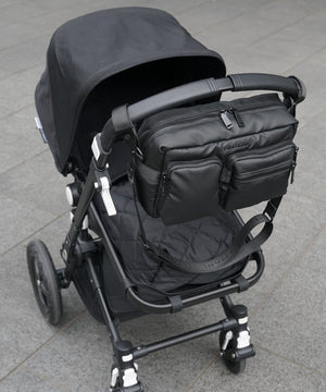 Black stroller with attached bag on a gray pavement