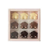 A 9-piece chocolate gift box featuring animal-shaped chocolates in three colors: pale cream, medium brown, and dark chocolate. The chocolates are shaped like sheep, cows, and pigs, with small white details on their faces.