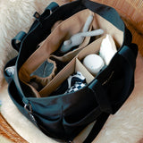 Black diaper bag with compartments containing baby items on a fluffy surface