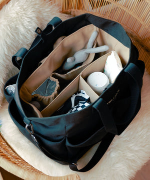 Black diaper bag with compartments containing baby items on a fluffy surface