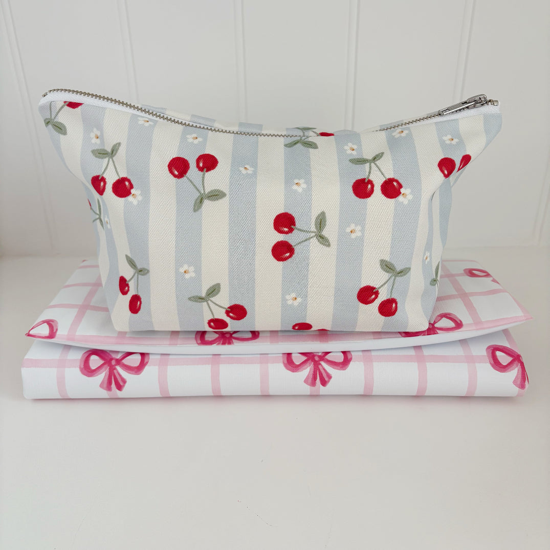 Nappy Wallet Cherry Stripe, front view sitting on top of two folded pink bow gingham changing mats